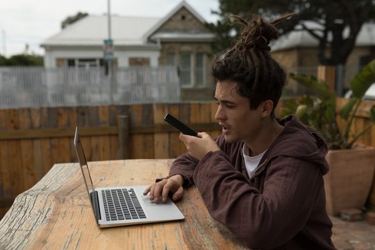 Male skateboarder talking on mobile phone while using laptop