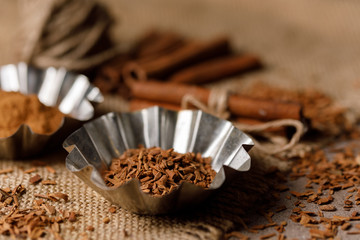 Shredded cinnamon in tins and cinnamon sticks on a textured background with textiles under the burlap.