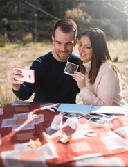 Pregnant woman and her husband makes a selfie with ultrasound image outside. Pregnancy, parenthood, preparation and expectation concept.