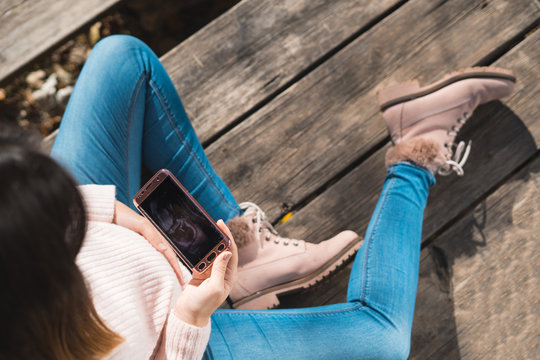 Top view of beautiful pregnant looking ultrasound image in her mobile phone.Concept of pregnancy, health care, gynecology, medicine. Young mother waiting of the baby.