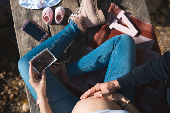 Top view of beautiful pregnant and her husband touching the tummy and looking ultrasound image. Concept of pregnancy, health care, gynecology, medicine. Young mother waiting of the baby.