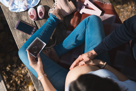 Top view of beautiful pregnant and her husband touching the tummy and looking ultrasound image. Concept of pregnancy, health care, gynecology, medicine. Young mother waiting of the baby.