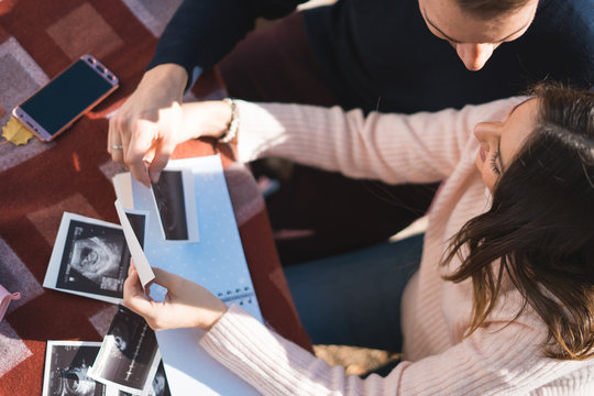 Pregnant woman and her husband makes notes in notebook and holding ultrasound image and medical documents. Pregnancy, parenthood, preparation and expectation concept.