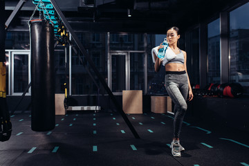 Fototapeta na wymiar athletic asian girl holding sports bottle with water at gym
