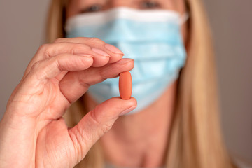 Woman wearing a mask holding a prescribed tablet between her thumb and forefinger.