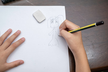 kids hand using pencil to draw cartoon on a white paper, close up