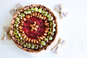 Tasty pink raspberry tart with grape and almonds on the white table.