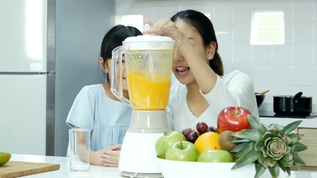 Mother and little using juice blender at kitchen. They making orange juice for drink. People with lifestyle and healthy concept.