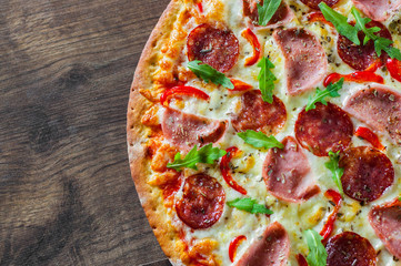 Pizza with Mozzarella cheese, ham, tomato sauce, salami, pepper, Spices and Fresh arugula. Italian pizza on wooden table background