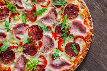 Pizza with Mozzarella cheese, ham, tomato sauce, salami, pepper, Spices and Fresh arugula. Italian pizza on wooden table background