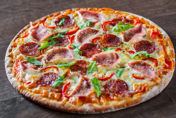 Pizza with Mozzarella cheese, ham, tomato sauce, salami, pepper, Spices and Fresh arugula. Italian pizza on wooden table background