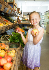 girl choosing apples in vegetable shop. on the signboard inscriptions in Catalan