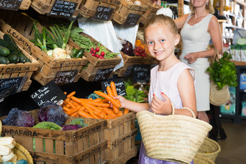 girl choosing  carrots in vegetable shop. on the signboard inscriptions in Catalan