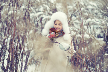 Little cute girl hide in high wet grass in snowy cold winter day playing with snowflakes