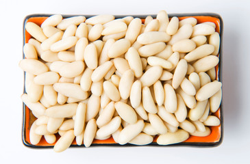 Peeled pine nuts in a ceramic bowl, on a white background.
