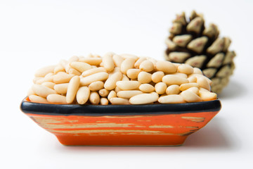 Peeled pine nuts in a ceramic bowl. Cone in the background