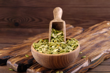 Pumpkin seeds with a bowl and scoop on a wooden background.