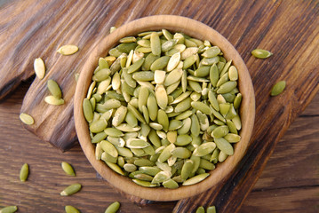 Pumpkin seeds with a bowl and scoop on a wooden background.