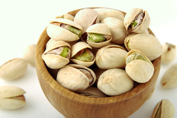 Salted pistachios in a wooden bowl on a white isolate.
