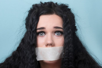 portrait of young woman with mouth and lips sealed in adhesive tape restrained and abused censored...