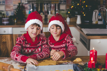 Sweet toddler child and his older brother, boys, helping mommy preparing Christmas cookies at home .