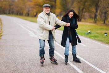 Fototapeta premium Happy pension. Active sport old people. The old man goes on rollers with his young daughter in the autumn park. Comic dance, a parody of the Swan Lake.