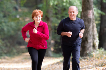 Senior couple wearing sportswear and running in forest