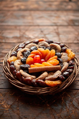 Mix of dried fruits in a small wicker basket on wooden table. Assortment contais apricots, plums, figs, dates, cherries, peaches. Above view with copy space.