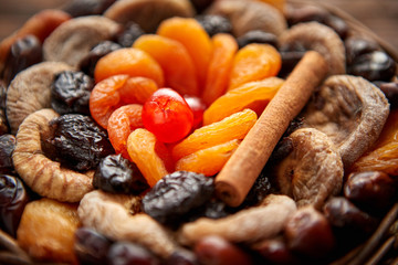 Close up of mix of dried fruits in a small wicker basket on wooden table. Assortment contais apricots, plums, figs, dates, cherries, peaches. Above view with copy space.
