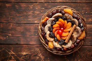 Mix of dried fruits in a small wicker basket on wooden table. Assortment contais apricots, plums, figs, dates, cherries, peaches. Above view with copy space.