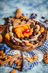 Composition of dried fruits and nuts in small wicker bowl placed on a stone table. Assortment contais almonds, walnuts, apricots, plums, figs, dates, cherries, peaches. Above view with copy space.