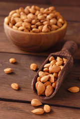 Dry apricot kernels in a wooden bowl and scoop on a wooden background.
