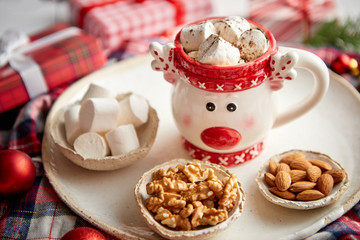 Delicious homemade christmas hot chocolate or cocoa with marshmellows in a red xmas decorative cup. With almonds, walnuts in small bowls on side