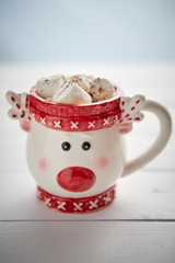 Tasty homemade christmas hot chocolate or cocoa with marshmellows in a red xmas decorative cup. Placed on white wooden background.