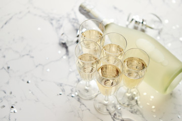 Champagne glasses and bottle placed on white marble background. Party and holiday celebration concept with confetti and serpentines. With copy space.
