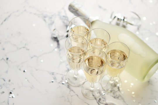 Champagne glasses and bottle placed on white marble background. Party and holiday celebration concept with confetti and serpentines. With copy space.