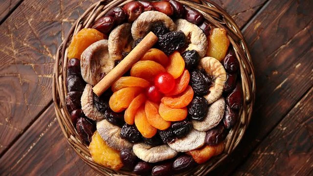 Mix of dried fruits in a small wicker basket on wooden table. Assortment contais apricots, plums, figs, dates, cherries, peaches. Above view with copy space.