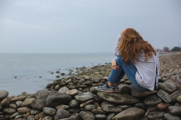 Young Upset and Depressed Woman Sitting on Rocks by the Sea with her Head in her Hand.