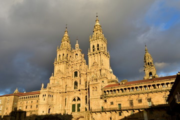 Fototapeta na wymiar Cathedral with sunset light. Obradoiro Square, rainy day, grey sky. Baroque facade and towers, Santiago de Compostela, Spain.