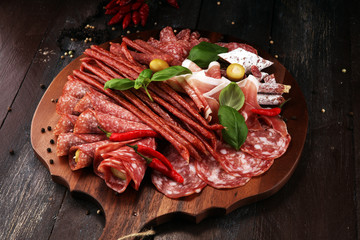 Food tray with delicious salami, pieces of sliced prosciutto crudo, sausage and basil. Meat platter with selection