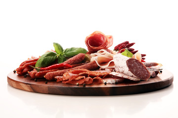 Food tray with delicious salami, pieces of sliced prosciutto crudo, sausage and basil. Meat platter with selection
