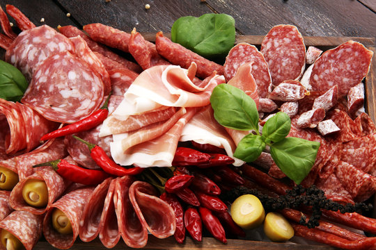 Food tray with delicious salami, pieces of sliced prosciutto crudo, sausage and basil. Meat platter with selection
