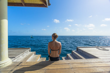 Junge Frau im Bikin sitzt an einer Treppe auf den Malediven und blickt ins Meer