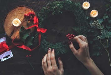 Female woman hands making DIY Yule winter solstice (Christmas) wreath from cedar evergreen tree...
