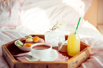 Breakfast in bed with i love you text on a note. Cup of coffee, juice, macaroons, rose flower and giftbox on wooden tray. Romantic breakfast in bed. Birthday, Valentine's day morning. Copy space.