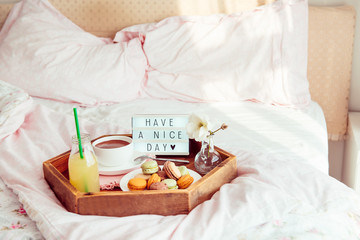 Breakfast in bed with Have a nice day text on lighted box. Cup of coffee, juice, macaroons, flower in vase on wooden tray. Good morning mood. Hospitality, care, service concept. Copy space.