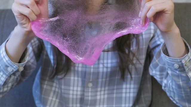 Woman is stretching a pink slime and playing. Close-up hands.