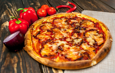 pizza on wooden table with ingredients, tomatoes, pepper, onion