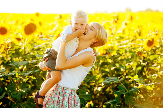 Portrait of mother and her cute child laughting in sunflower surroundings