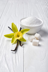 White granulated and cubes sugar with vanilla yellow flower and sticks